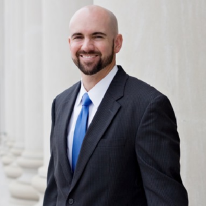 Man in suit smiling near white columns.